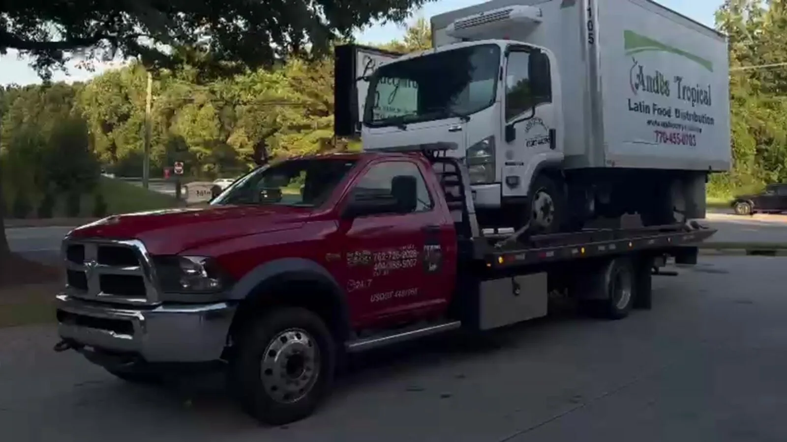 Red flatbed tow truck transporting a refrigerated box truck