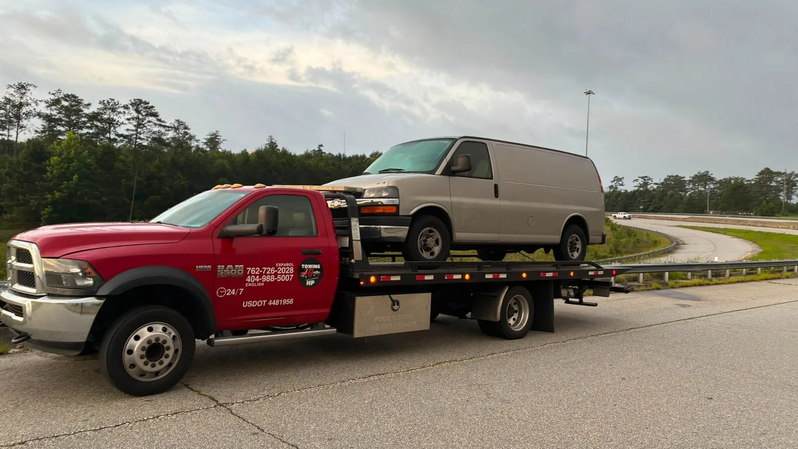 Red flatbed tow truck transporting a cargo van near an Atlanta highway
