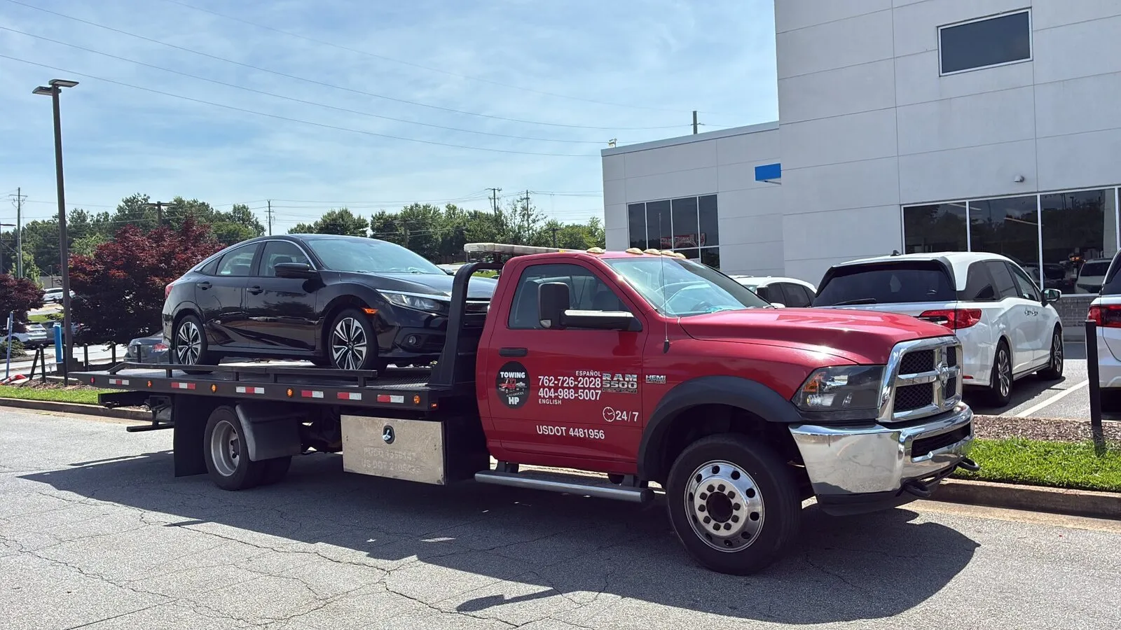 Red flatbed tow truck transporting a black sedan